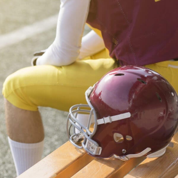 American football player sitting on bench and helmet next to him